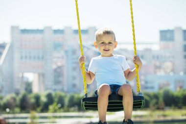 Küçük çocuk kameraya bakar ve Bahçesi Şehir parkta salıncağa bir güneşli yaz gününde sahiptir yakın çekim