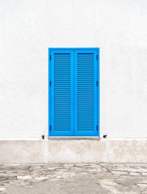 Santorini güneşli bir Yunan tarzında beyaz bir duvar üzerinde mavi panjurlar ile bir pencere.