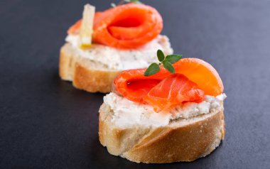 Siyah arka planda iki küçük somon sandviçi.