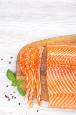 Çiğ taze somon filetosu dilimlenmiş ve ahşap tahtada fesleğen ve baharatla dilimlenmiş.