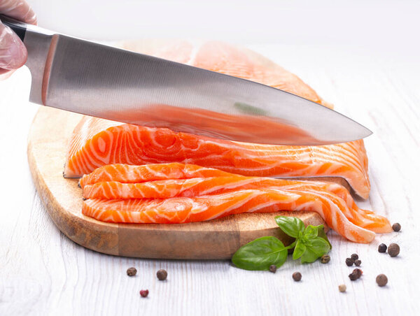 Нож режет ломтики свежего лосося на деревянной доске