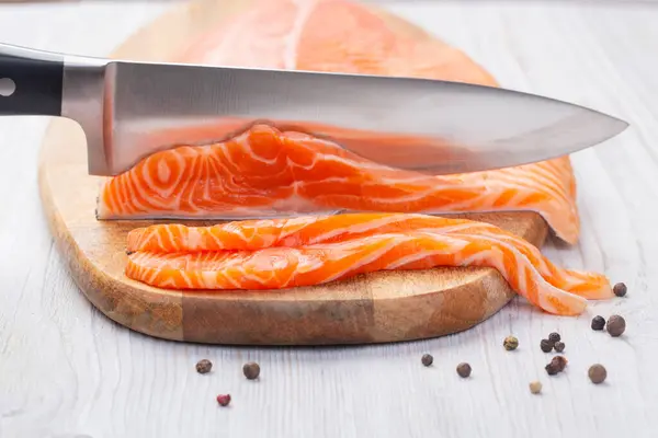 Knife cuts slices of fresh raw salmon on wooden board