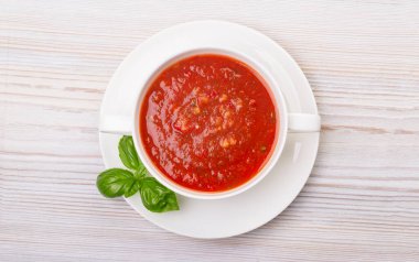 Beyaz bir tabakta gazpacho ve ahşap beyaz bir masada fesleğen.