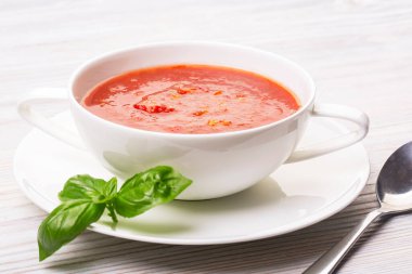 Beyaz bir tabakta gazpacho ve ahşap beyaz bir masada fesleğen.