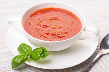 Beyaz bir tabakta gazpacho ve ahşap beyaz bir masada fesleğen.