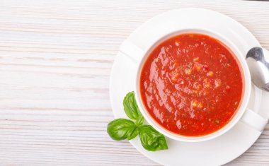 Beyaz bir tabakta gazpacho ve ahşap beyaz bir masada fesleğen.