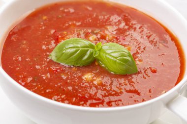 Beyaz bir tabakta gazpacho ve ahşap beyaz bir masada fesleğen.