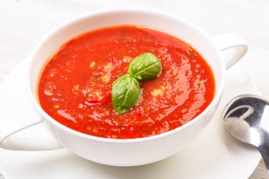 Beyaz bir tabakta gazpacho ve ahşap beyaz bir masada fesleğen.