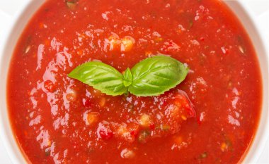 Beyaz bir tabakta gazpacho ve ahşap beyaz bir masada fesleğen.