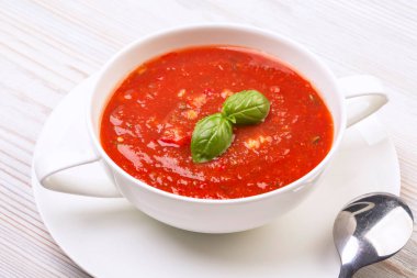 Beyaz bir tabakta gazpacho ve ahşap beyaz bir masada fesleğen.