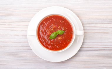 Beyaz bir tabakta gazpacho ve ahşap beyaz bir masada fesleğen.