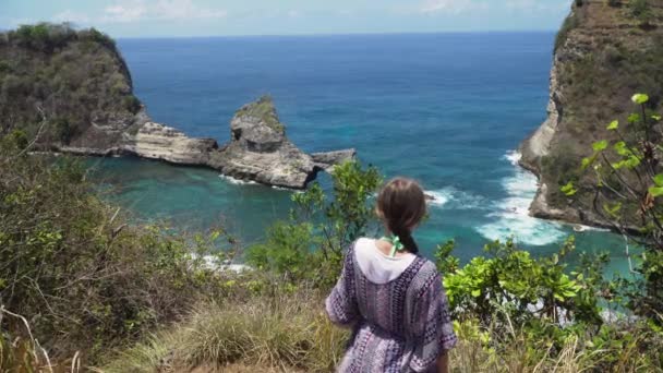 Menina de pé em um penhasco e olhando para o mar. Bali, Indonésia — Vídeo de Stock