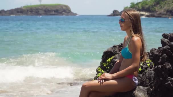 A rapariga senta-se na rocha e olha para o mar. Bali, Indonésia — Vídeo de Stock