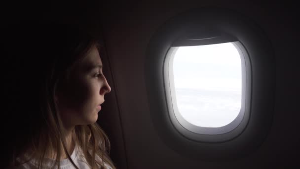 Chica sentada junto a la ventana del avión y mirando afuera. — Vídeos de Stock