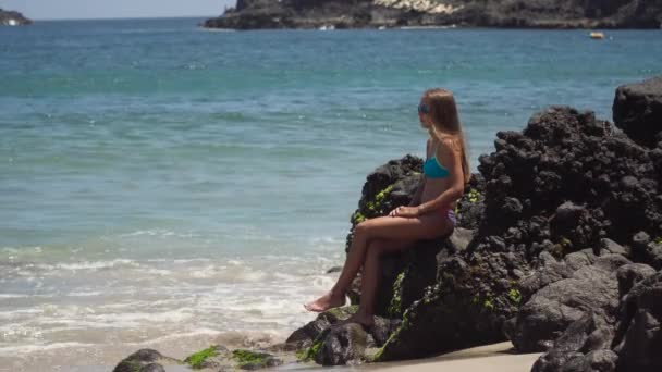 少女は岩の上に座って海を見る。インドネシアのバリ — ストック動画