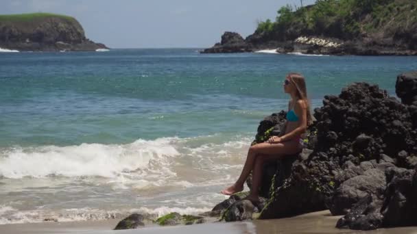 Девушка сидит на скале и смотрит на море. Бали, Индонезия — стоковое видео