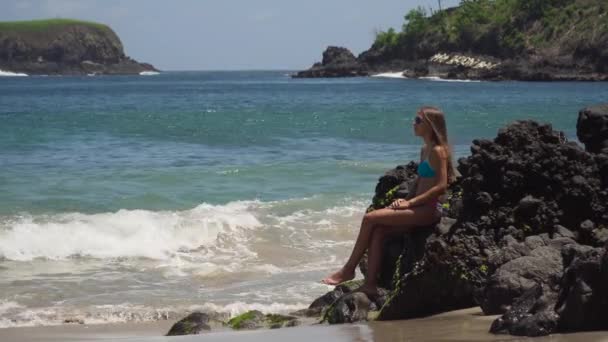 A rapariga senta-se na rocha e olha para o mar. Bali, Indonésia — Vídeo de Stock