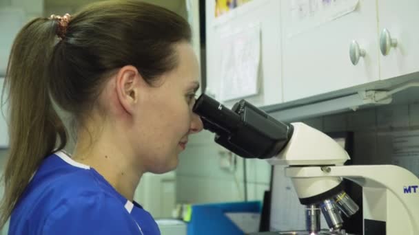 Médico mujer mira en un microscopio. — Vídeos de Stock