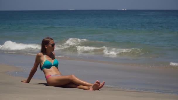 戴着太阳镜的女孩坐在海滩上. — 图库视频影像