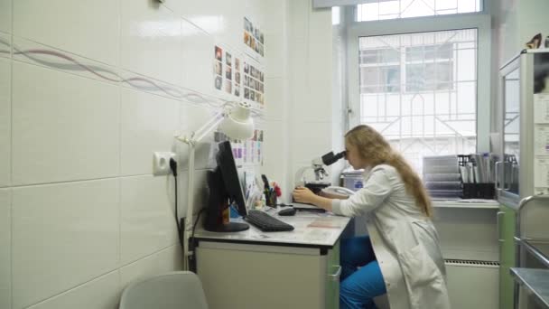 Médico mujer mira en un microscopio. — Vídeos de Stock