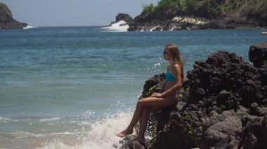 Kız kayaya oturur ve denize bakar. Bali, Endonezya