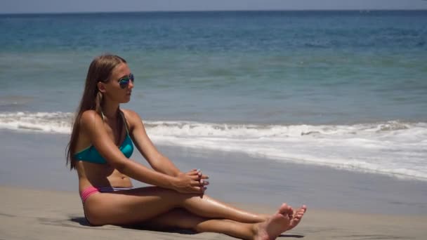 Menina nos óculos de sol senta-se na praia. — Vídeo de Stock