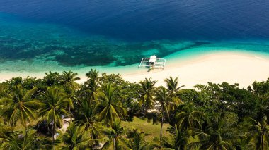 Beyaz kumdan oluşan tropik plaj, üst manzara. Sahilde bir turist teknesi. Sakin plaj sahnesi.