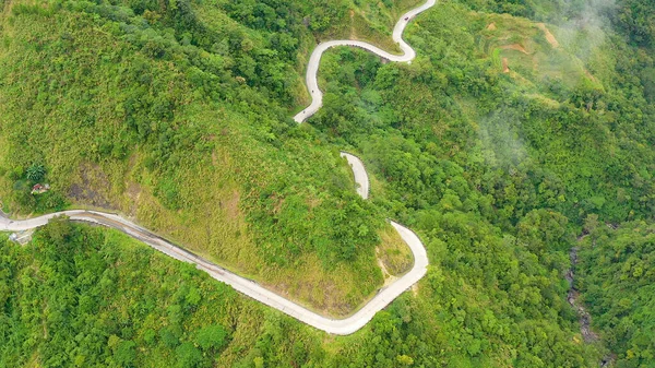 Estrada curva de montanha passando ao longo das encostas das montanhas e colinas cobertas com floresta verde e vegetação. Filipinas, Luzon. — Fotografia de Stock