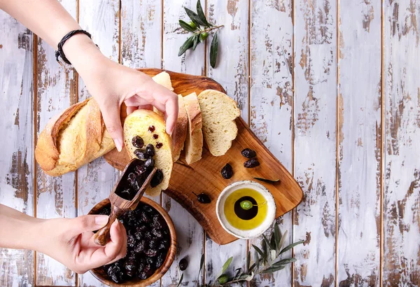 女性手服务传统的希腊开胃橄榄与面包 橄榄油和醋 在质朴的橄榄木板上的白色木质背景 顶部视图 — 图库照片