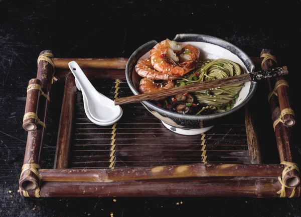 Green tea soba noodles  served with shrimps,  shiitake mushrooms and spicy broth on a vintage bamboo tray.