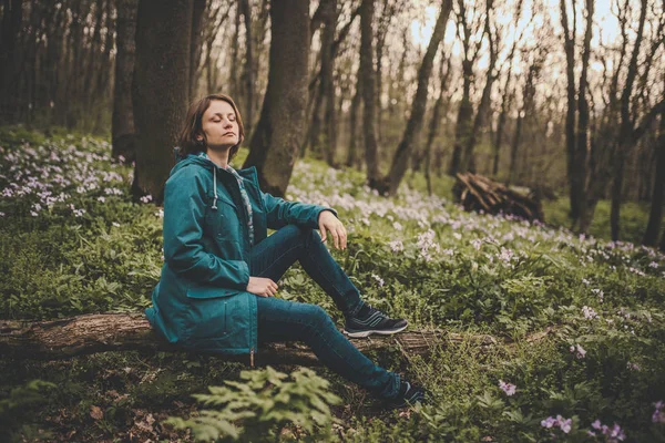 Toned photo of happy hiking middle-aged woman in blue jacket sitting and resting in evening spring forest — Stock Photo, Image
