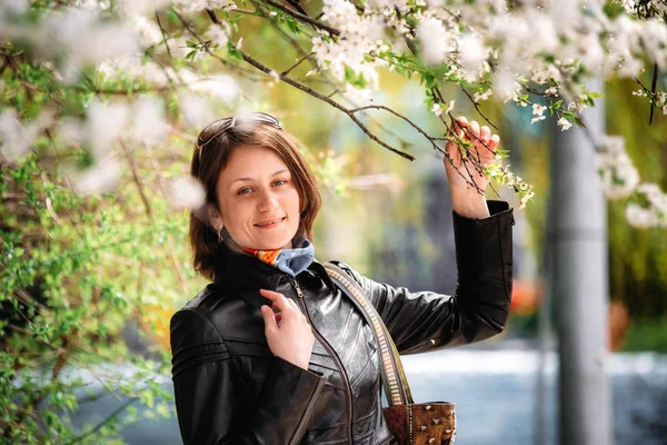 Siyah deri ceket ayakta çiçek açan ağacında mutlu orta yaşlı kadın fotoğrafı — Stok fotoğraf