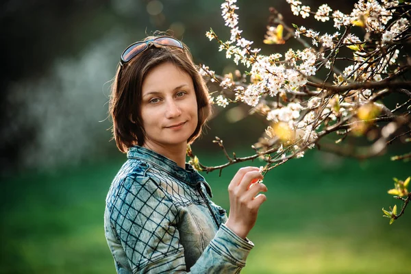 Mavi ceket ve ayakta çiçek açan ağacının dalını yakınındaki mutlu orta yaşlı kadın fotoğrafı — Stok fotoğraf