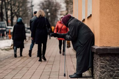 Photo of old hungry homeless female beggar beg for alms and on street. clipart