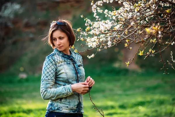 Фото счастливой женщины средних лет в синей куртке, стоящей возле ветки цветущего дерева — стоковое фото