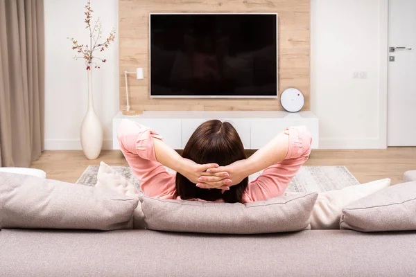 Yalnız üzücü depresif güzel genç kadın kanepede oturan ve Tv izlerken lüks daireler arkadan görünüm.