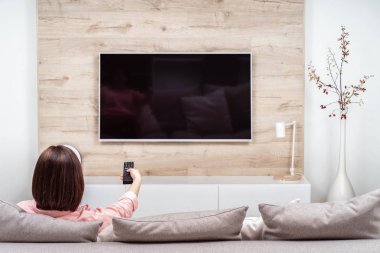 Arkadan görünüşü kanal değiştirme Tv izlerken yalnız hüzünlü depresif genç kadın kanepe, oturma lüks daireler.