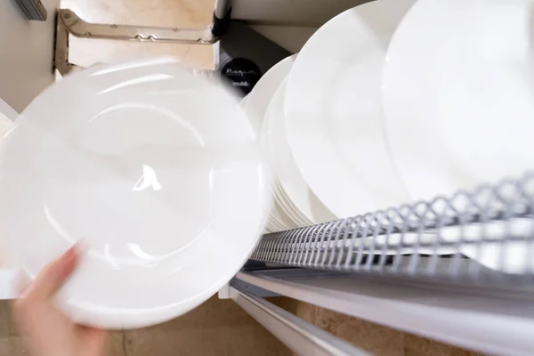 Woman holding in hand plate and getting out or putting in it in kithen or dishwasher shelf. — Stock Photo, Image