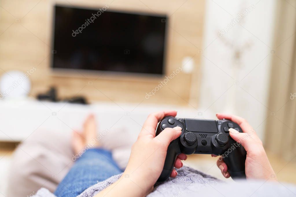 POV Woman lying on the coach in front of TV and holding in hands wireless game controller. Game addiction concept.