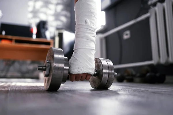 Wide angle photo of broken fractured hand in plaster cast holding dumbbell. Home trainig rehabilitaion after accident. — Stock Photo, Image