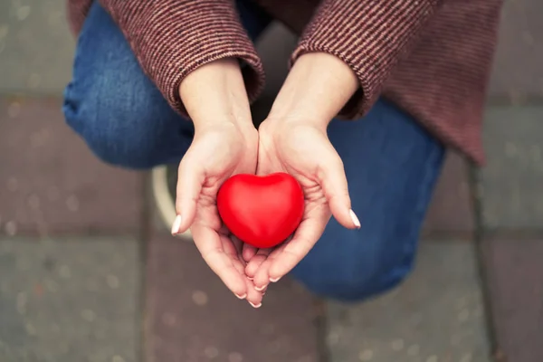 Een vrouw met een rood hart die op de knieën blijft. Verklaring van liefde of liefdadigheid concept. — Stockfoto