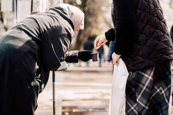 Photo of passerby givining alms for old hungry homeless female beggar on street — Stock Photo, Image