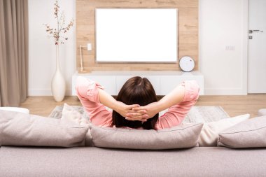 Arkadan görünüşü güzel genç kadın lüks appartments dinlenme, kanepede oturan ve Tv izlerken.
