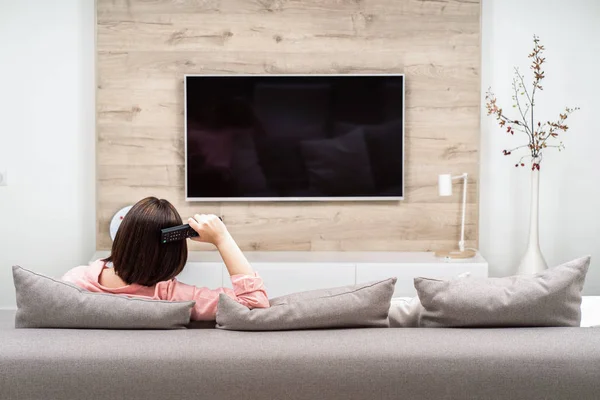 Arkadan görünüşü güzel genç kadın lüks appartments dinlenme, kanepede oturan ve Tv izlerken.