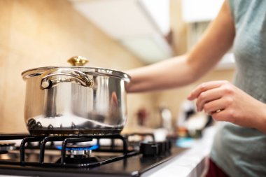 Gaz-ocakta ayakta yemek, elleri büyük çelik tencere, ambarda prepairing güzel genç kadın ev kadını.