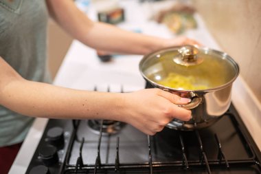 Gaz-ocakta ayakta yemek, elleri büyük çelik tencere, ambarda prepairing güzel genç kadın ev kadını.