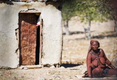 Damaraland Namibya - 21 Mayıs 2018; Mat kulübe dışında geleneksel kolye ve süslemeler ile kabile kadın oturur.