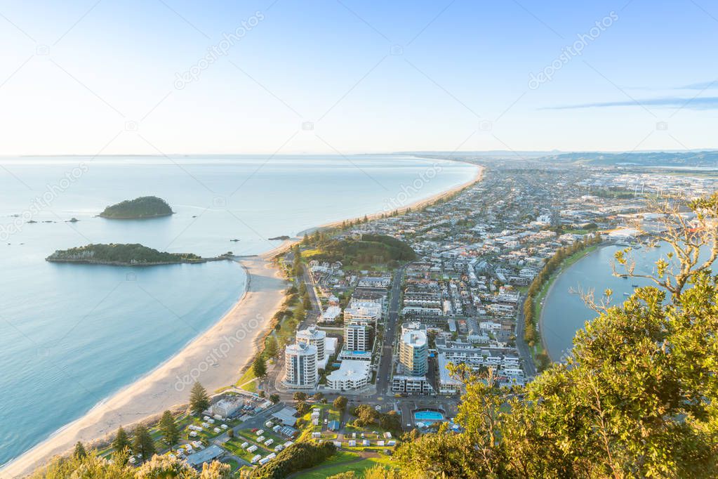 Mount Maunganui stretches south out below as sun rises on horizon and falls across ocean beach and buildings below