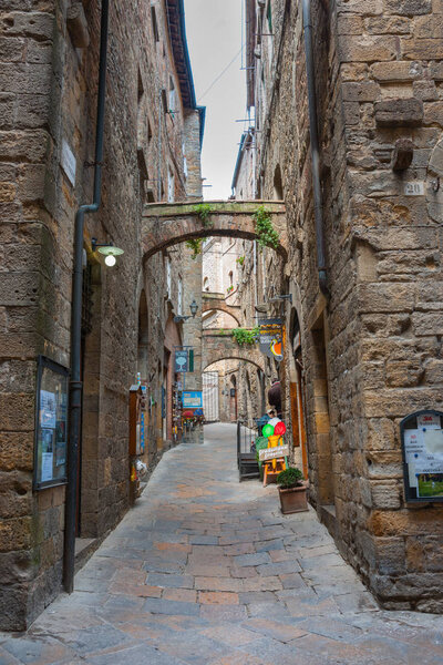 VOLTERA ITALY - APRIL 21 2011; Narrow laneway lined by high stone buildings with small business and cafes