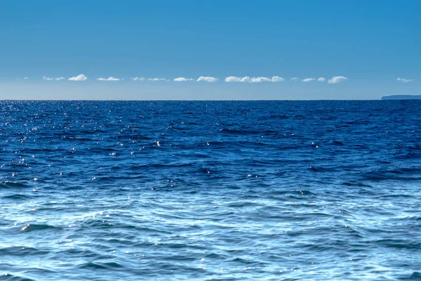 Thin white cloud above distant horizon blue sky and sea tones blending with sun sparkles on water ideal use as background image